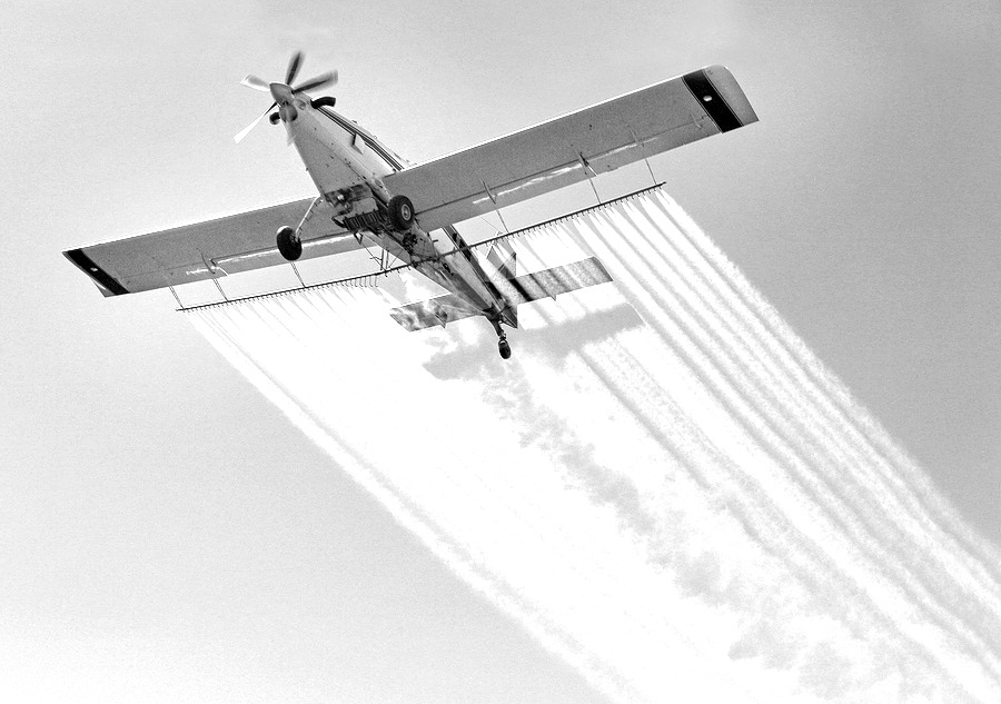 Airplane spraying insecticides over a farm field Airplane spraying insecticides over a farm field