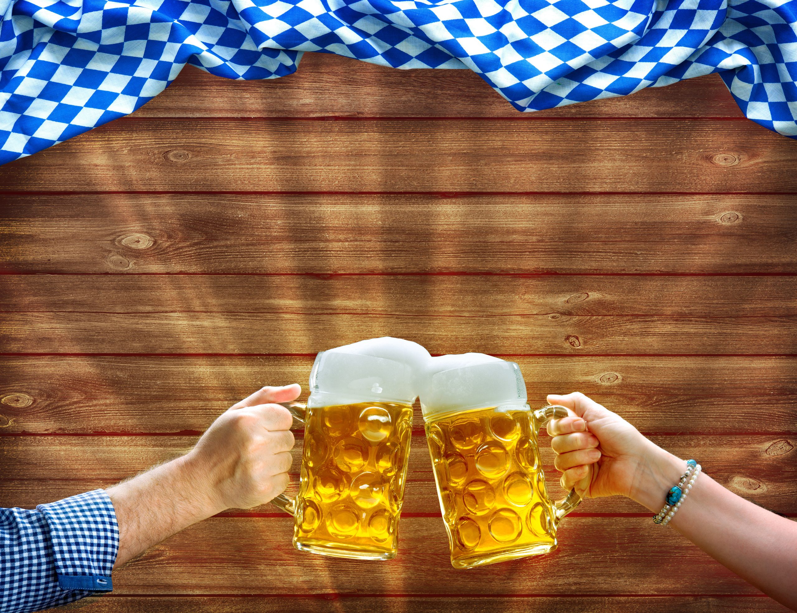 Hands holding up beer mugs under Bavarian flag Hands holding up beer mugs under Bavarian flag