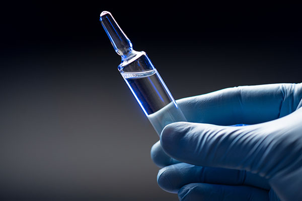 Hand in blue medical gloves holds an ampoule with a coronavirus vaccine.